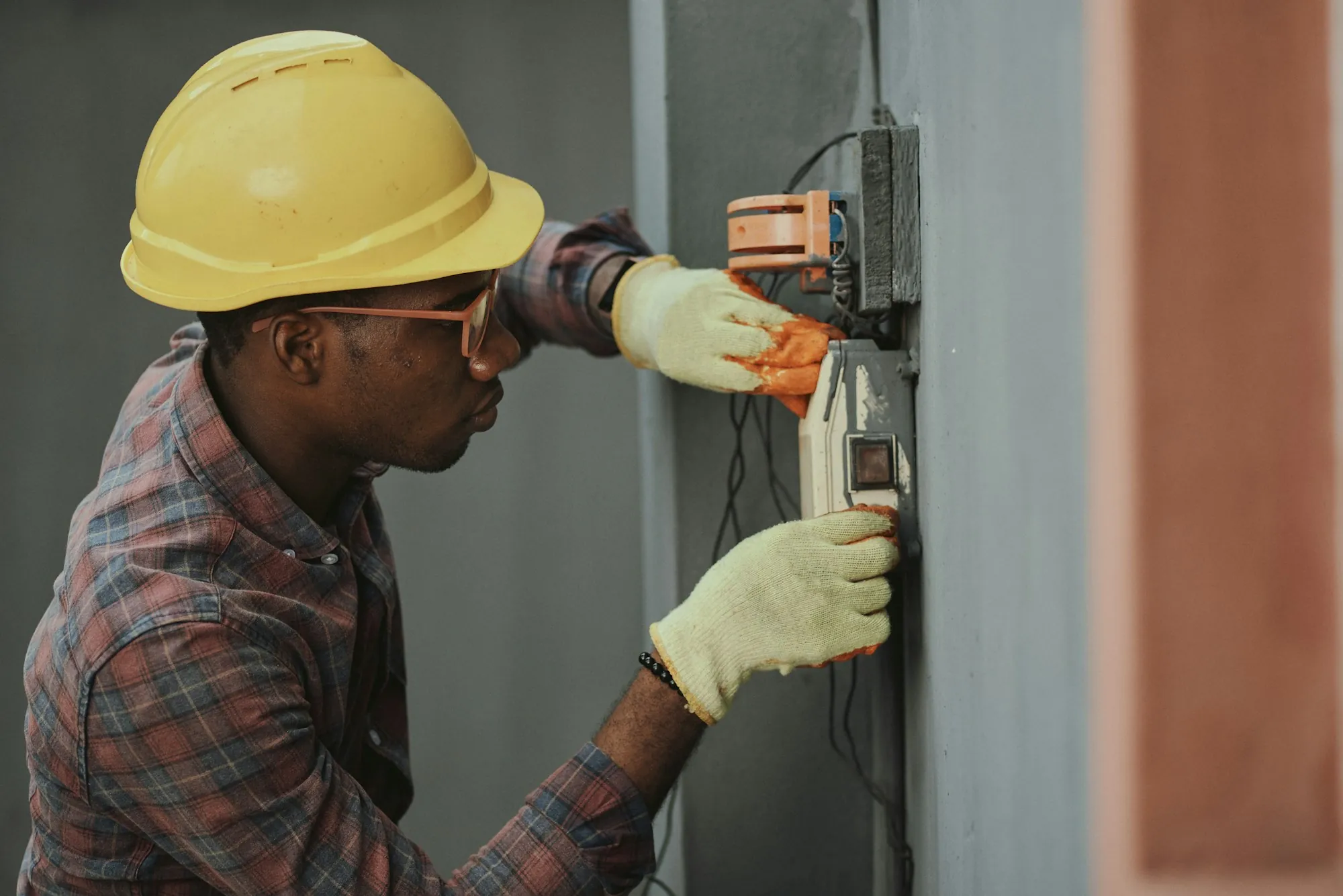 Technician in a hard hat testing a wall panel with a meter